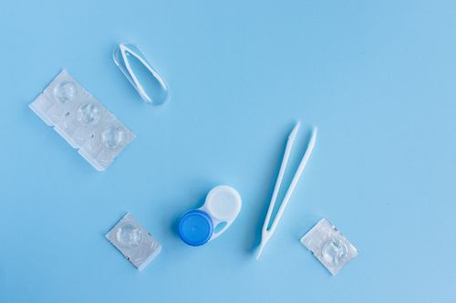 Free Flat lay of contact lens accessories including case and tweezers on a blue background. Stock Photo