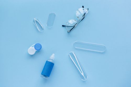 Free Flat lay of contact lens case, solution, and glasses on a blue background. Stock Photo