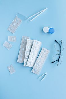 俯视图中，隐形眼镜、眼镜和镊子置于淡蓝色背景上