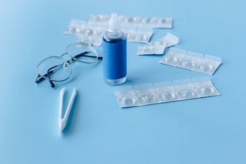 Free Close-up of contact lens solution bottle with eyeglasses and tweezers on blue backdrop. Stock Photo
