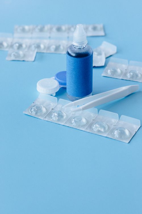 Free A close-up of contact lens care items including solution, blister packs, and tweezers on a blue background. Stock Photo