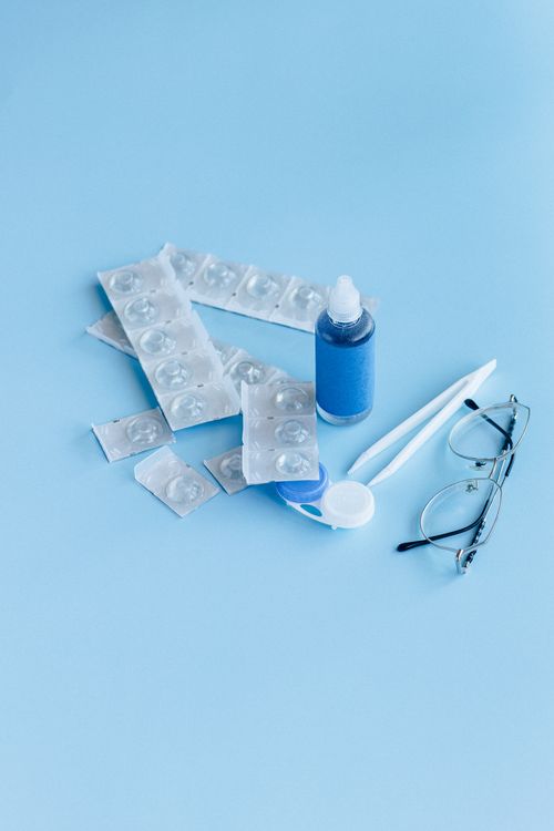 Free Close-up of contact lens care items including solution, case, and glasses on a blue backdrop. Stock Photo
