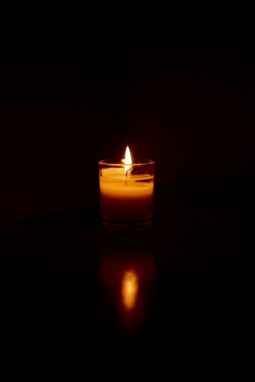 Free A single candle illuminating darkness with a warm, reflective glow in a serene setting. Stock Photo