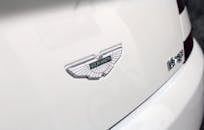 A close-up shot of the Aston Martin logo on a white luxury car's surface, highlighting elegance.