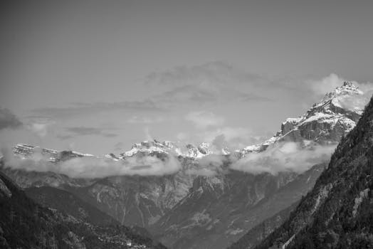 Dramatic black and white landscape of mountain range with snow-capped peaks and clouds.