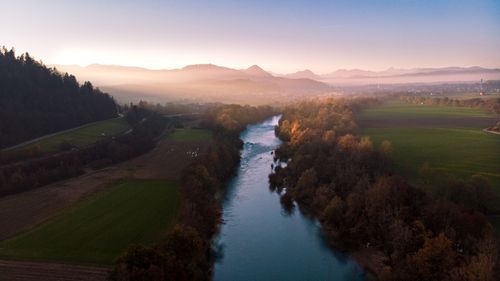 Free A tranquil aerial view of a river winding through misty fields, flanked by mountains at dawn. Stock Photo