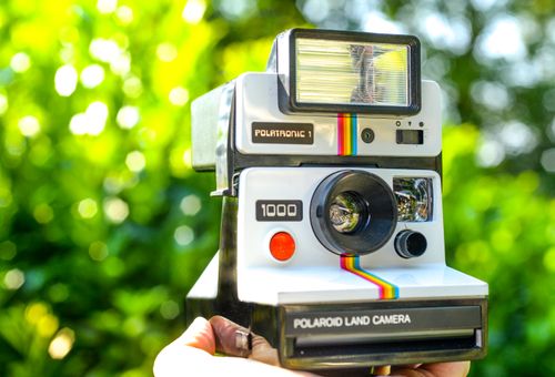 Free Close-up of a classic Polaroid Land camera against a vibrant outdoor background. Stock Photo