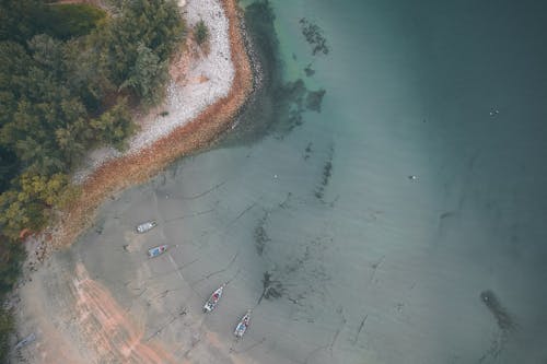 Drone top view of calm bay with boats moored on clean transparent water near sandy shore in exotic island