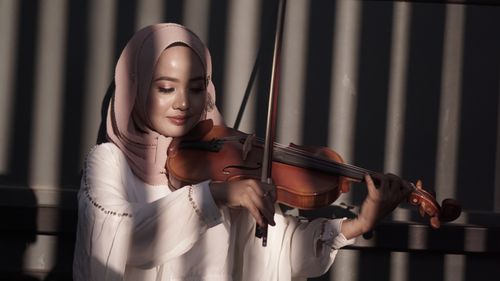 Free A woman in a hijab playing a violin indoors, enveloped in warm lighting. Stock Photo