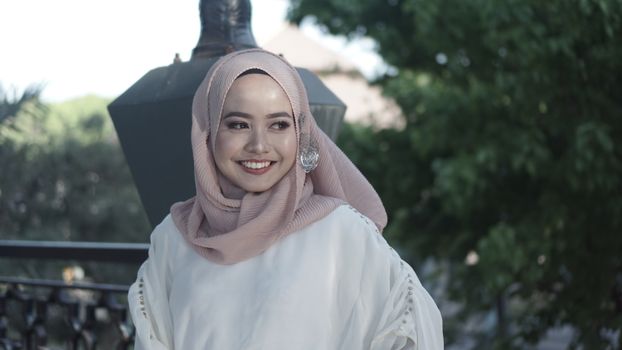 一位头戴头巾的快乐女子，在绿树成荫的户外微笑着