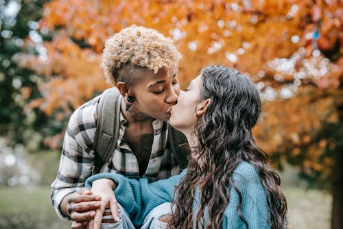 Free Romantic Hispanic woman and African American girlfriend caressing each other while spending time in nature with trees on blurred background Stock Photo