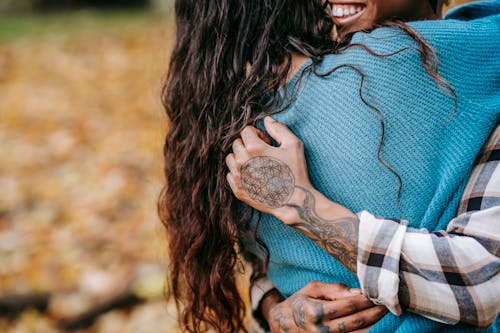 Free Unrecognizable African American tattooed person embracing anonymous girlfriend with dark hair during romantic date while standing in nature on autumn day Stock Photo