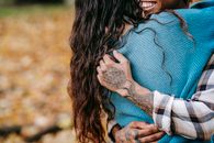 Unrecognizable African American tattooed person embracing anonymous girlfriend with dark hair during romantic date while standing in nature on autumn day