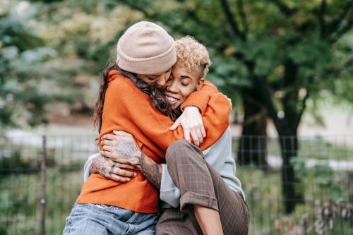Free Cheerful multiracial homosexual couple with closed eyes embracing each other while spending time on street near fence on blurred background Stock Photo