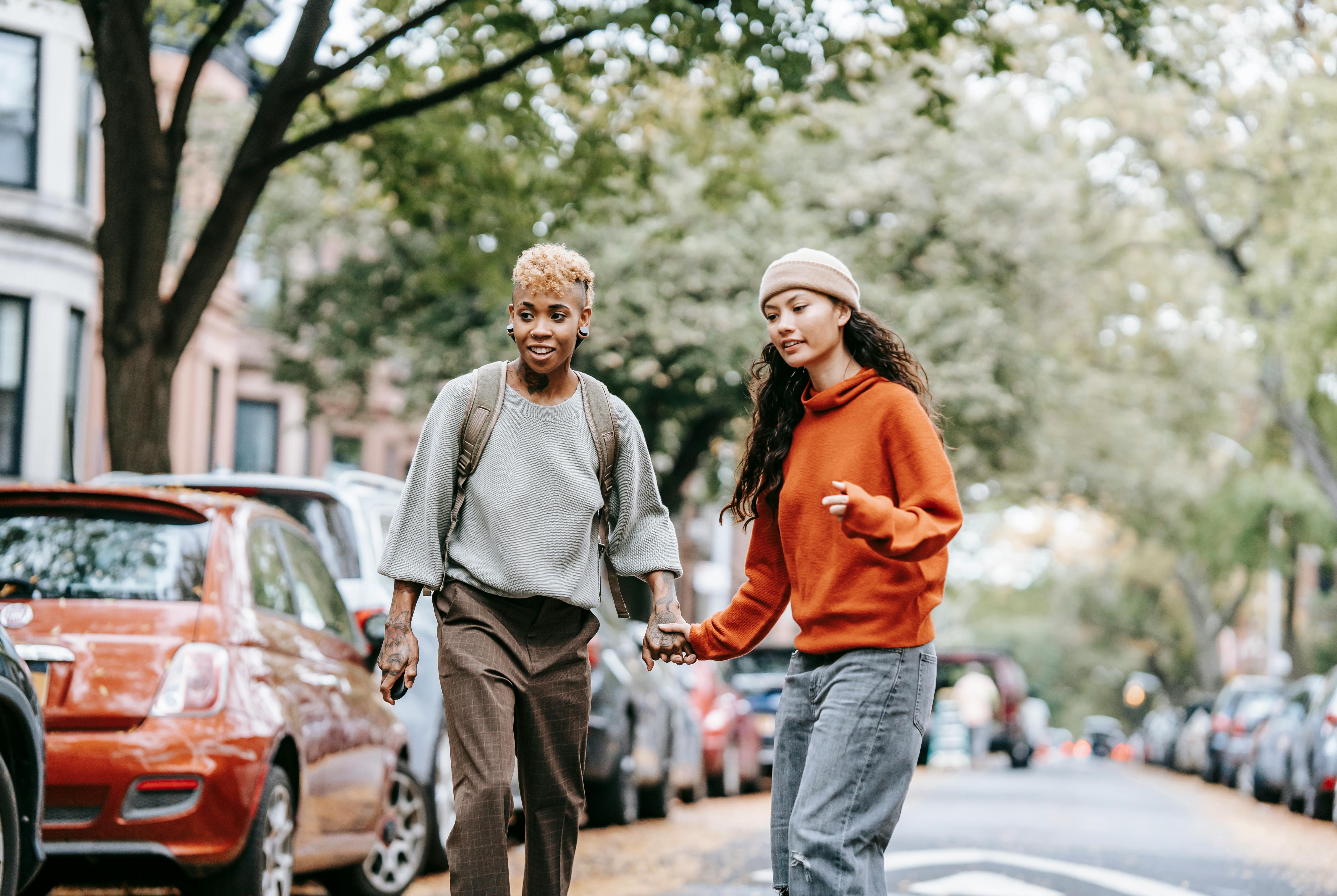 positive young gay couple walking along city street