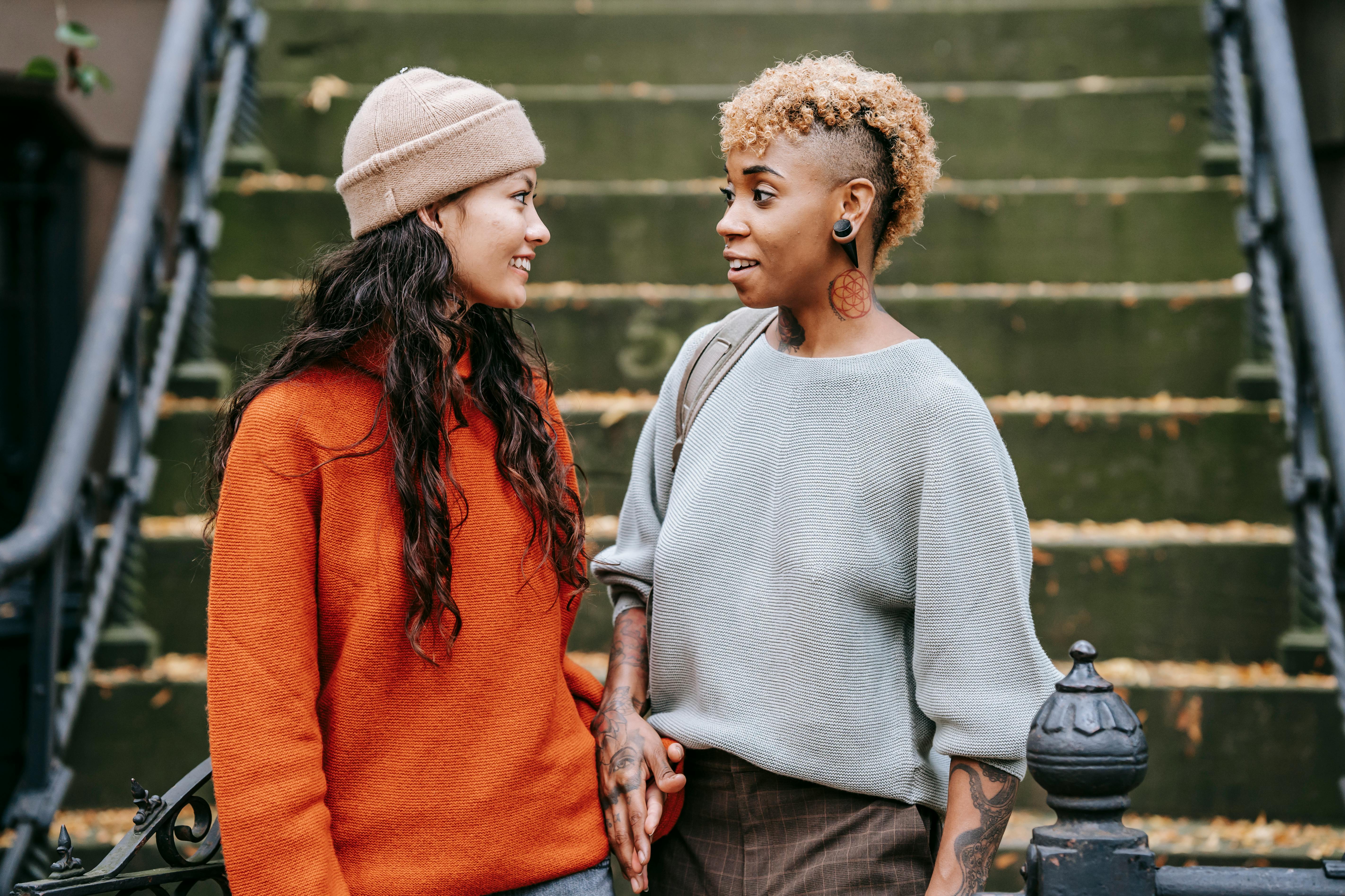 delighted multiethnic lesbian couple talking while standing near staircase