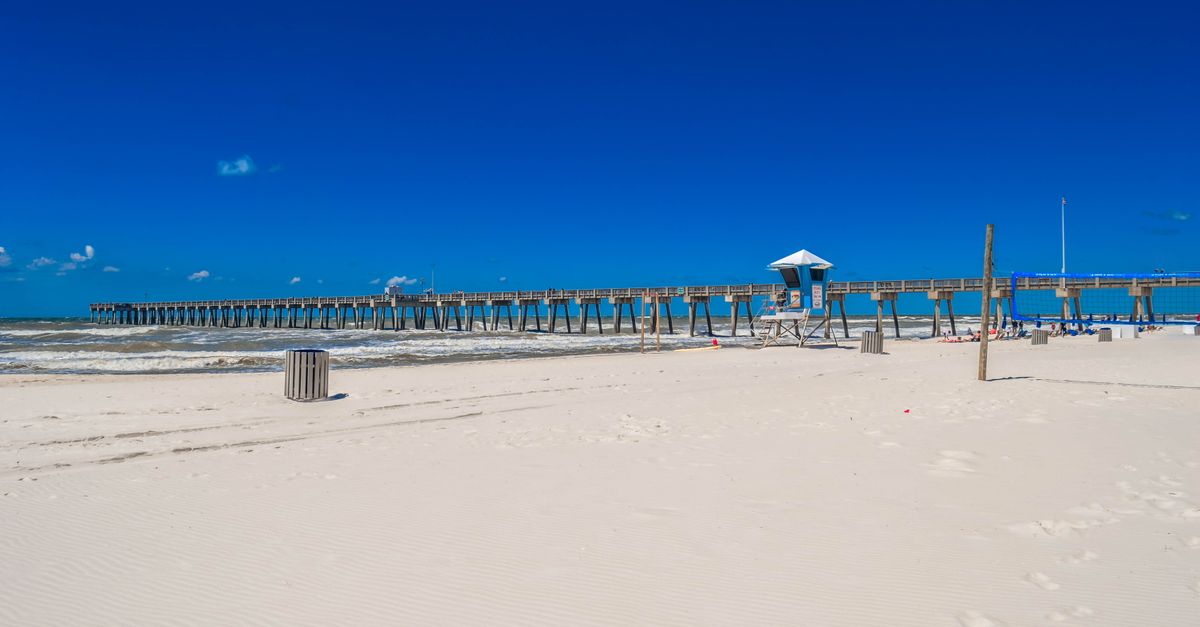 Pristine white sandy beach with a scenic pier under a clear blue sky in Panama City Beach, Florida.