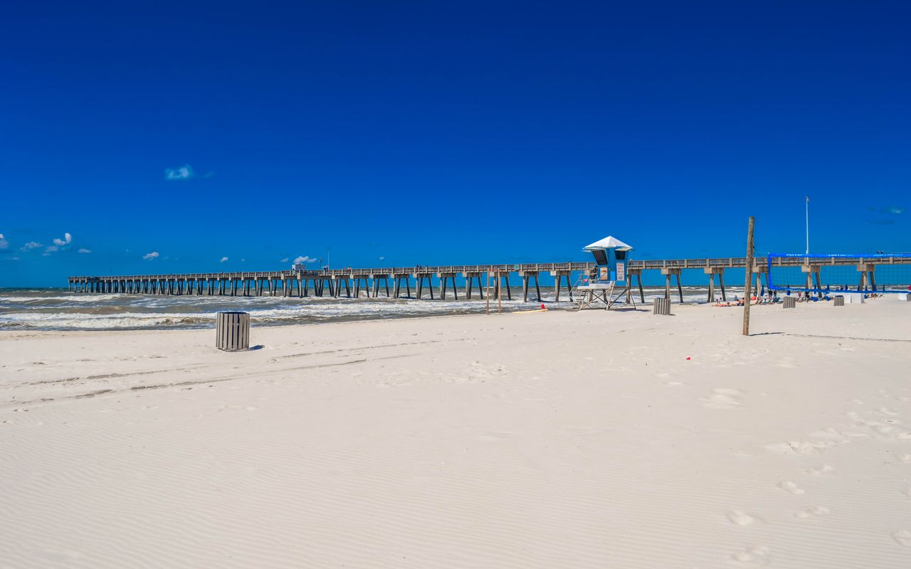 Pristine white sandy beach with a scenic pier under a clear blue sky in Panama City Beach, Florida.