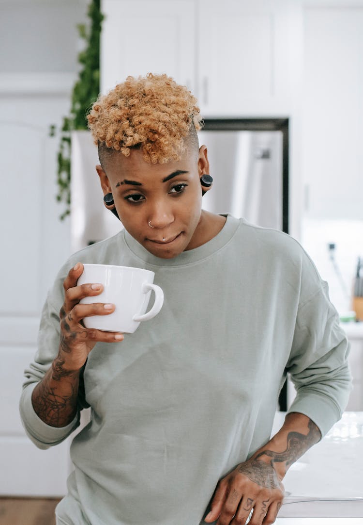 Thoughtful Young Black Woman Standing In Kitchen And Drinking Coffee