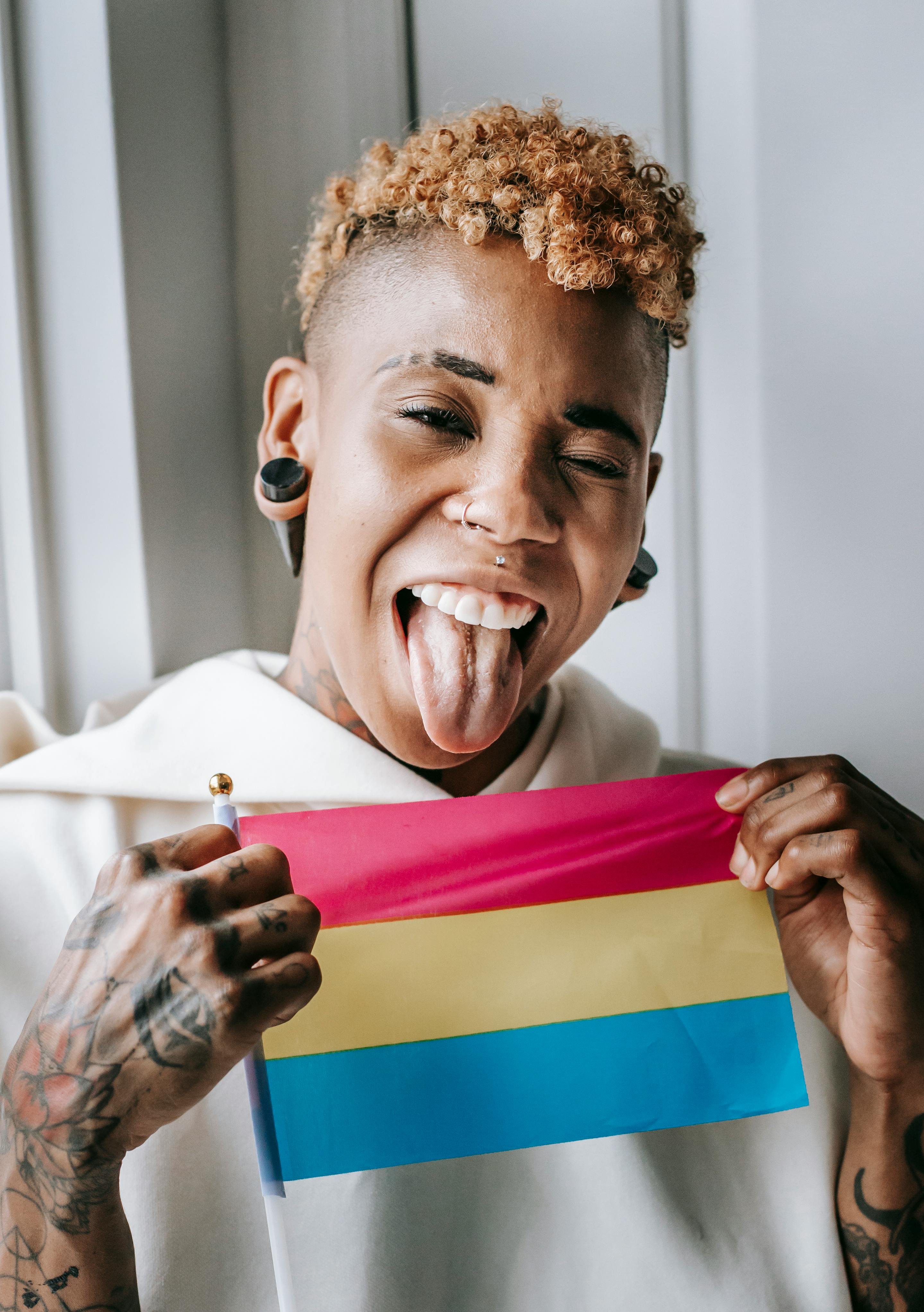 black woman with tongue out winking and showing pansexual pride flag
