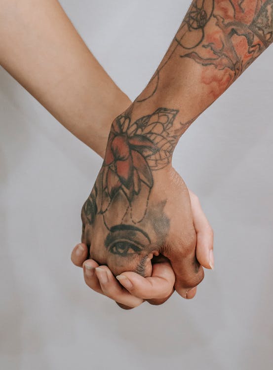 Young female hand holding other ethnic person hand with tattoos on gray background