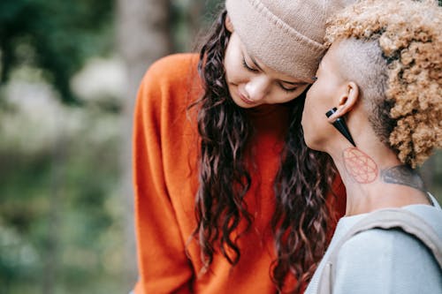 Free Young African American woman with tattoos on neck caressing with lesbian partner in warm cloth while spending time together Stock Photo