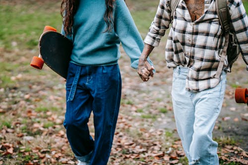 Crop young couple holding hands while walking with skateboards