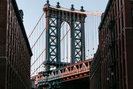 From below of bridge with metal heavy arch near concrete buildings under cloudless blue sky
