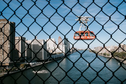 View through metal fence on ropeway above calm river located in city in sunny day