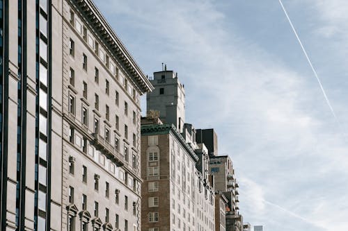 From below of contemporary apartment buildings with windows and terrace on roof under blue sky with clouds