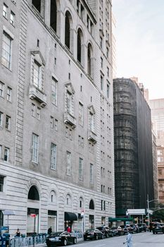 公寓楼的灰色外观带有拱形窗户，坐落在城市现代房屋附近，街道上停放的汽车上方是万里无云的天空