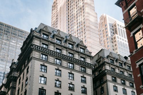 Free From below of residential building with white exterior and ornamented windows located near skyscraper against blue sky in city street Stock Photo