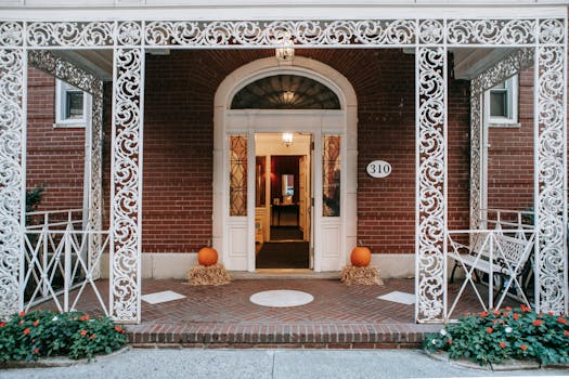 Exterior of residential brick building with doorway and white ornamental veranda with metal barriers located on street with blooming flowers