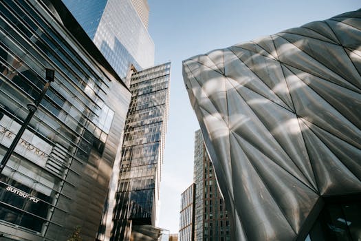 From below of contemporary office center with transparent walls located near futuristic building against blue sky in city on street