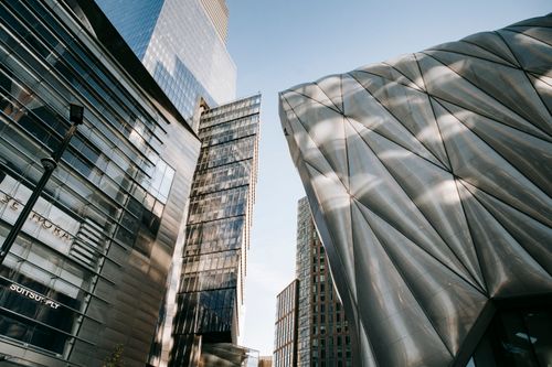 Free From below of contemporary office center with transparent walls located near futuristic building against blue sky in city on street Stock Photo