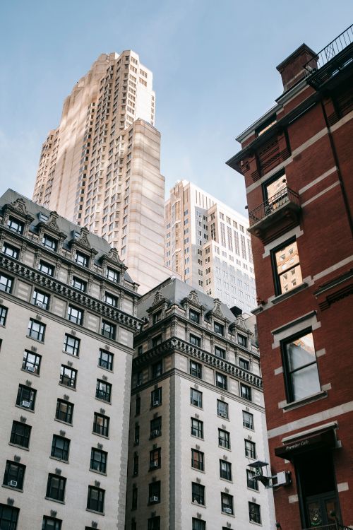 Free From below of residential white houses with geometric roof cornice located near contemporary building against blue sky in city street Stock Photo