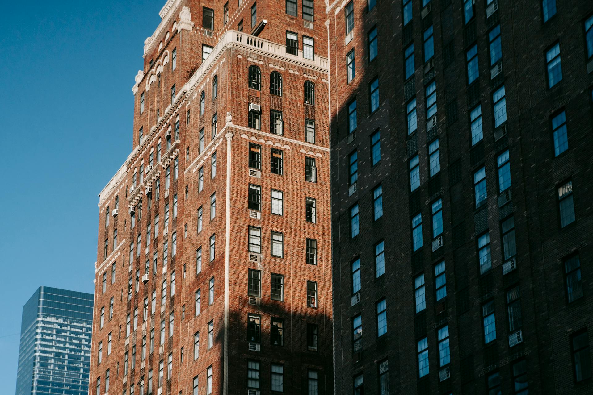 Low angle of residential multistory brown house under sunlight and shadow on wall against blue sky on city in street