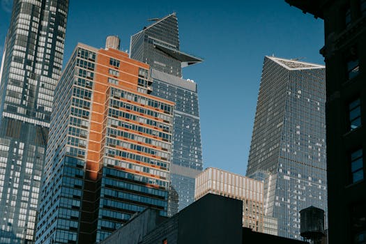 From below of contemporary high buildings with glass windows and modern design located against blue sky in city on street