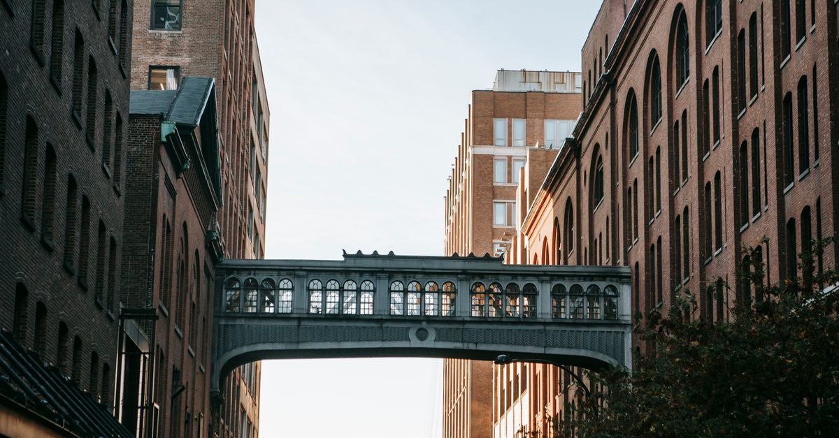Narrow street with metal overpass connecting brick apartment houses against cloudless sky in city street in residential area on sunny day