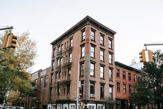 View of a classic brick apartment building on a city corner with trees and traffic lights.