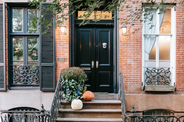 Entrance of residential building with pumpkins on stone stairway near black door and windows on brick wall located in street