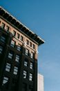From below of corner of apartment building with roof cornice located against blue sky in city on street in sunlight