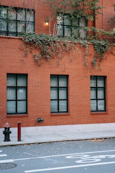 Facade of residential brick house with foliage on balconies aboe road in city in daylight