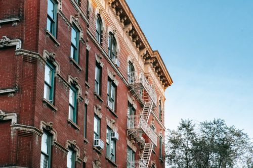 Free Low angle of exterior of aged brick apartment on background of blue sky and tree crown in city in soft daylight Stock Photo