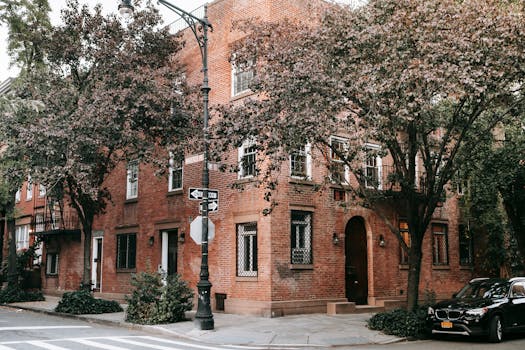 A quaint brick house surrounded by trees on a peaceful city street corner. by Charles Parker