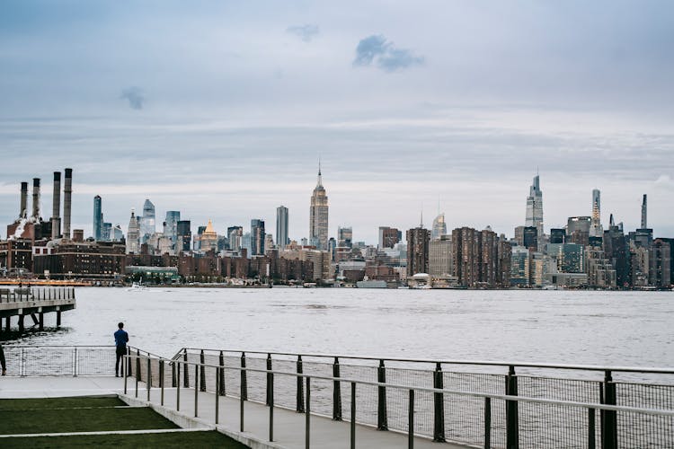 Man Standing On Embankment Of River In Big City