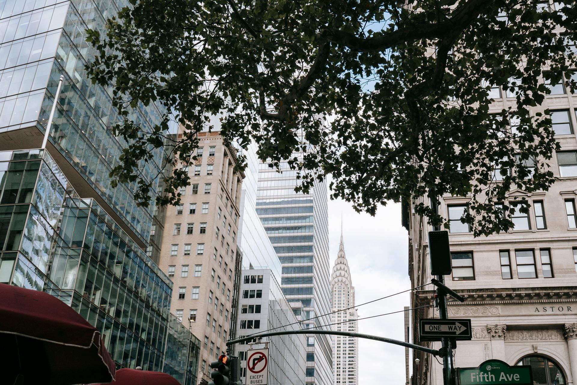 View of the Chrysler Building from Fifth Avenue, NYC, with modern skyscrapers and greenery.