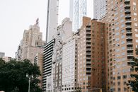 绿树映衬着金融区万里无云的天空，住宅楼立面位于城市街道上，靠近现代摩天大楼