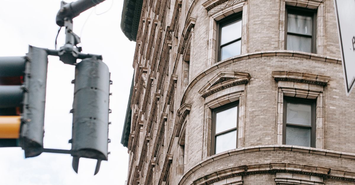 From below corner of stone apartment building with windows located on street in city with traffic light against cloudless sky