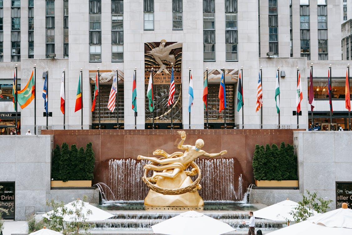 Golden Prometheus statue located near entrance of Rockefeller center with flags on street in New York city in modern district